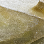 Brush wetting out a fresh layer of chopped strand mat over several glossy amber layers stacked on a boat edge, showing how layer thickness builds