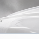An orbital sander smoothing a glossy white fiberglass hull to a mirror finish
