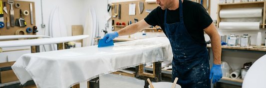 Spreading water-clear polyester laminating resin over fiberglass cloth on a surfboard blank