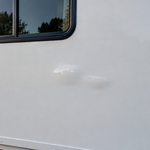 Small bubble in a white fiberglass RV sidewall below a window