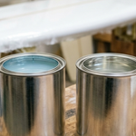 Two quart cans of clear polyester surfboard resin on a workbench, one with a faint blue tint