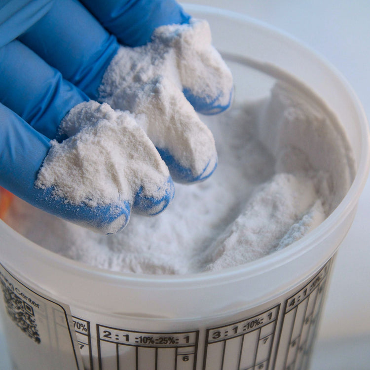 Gloved hand scooping white resin filler powder from a mixing tub, fillers and additives for epoxy