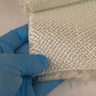 Gloved hand holding 40oz fiberglass E cloth to show its thickness, heavy white woven glass fabric with frayed cut edge.