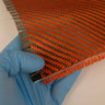 Gloved hand holding 5.5oz carbon Kevlar hybrid fabric, red Kevlar and black carbon fiber 2x2 twill weave with frayed edge.