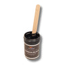 Wood stir stick coated in Carbon Black liquid pigment standing in the open 1 oz jar, showing the opaque black colorant for resin.
