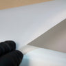 Black-gloved hand peeling a sheet of white peel ply release fabric off the roll, the fine weave visible along the lifted edge