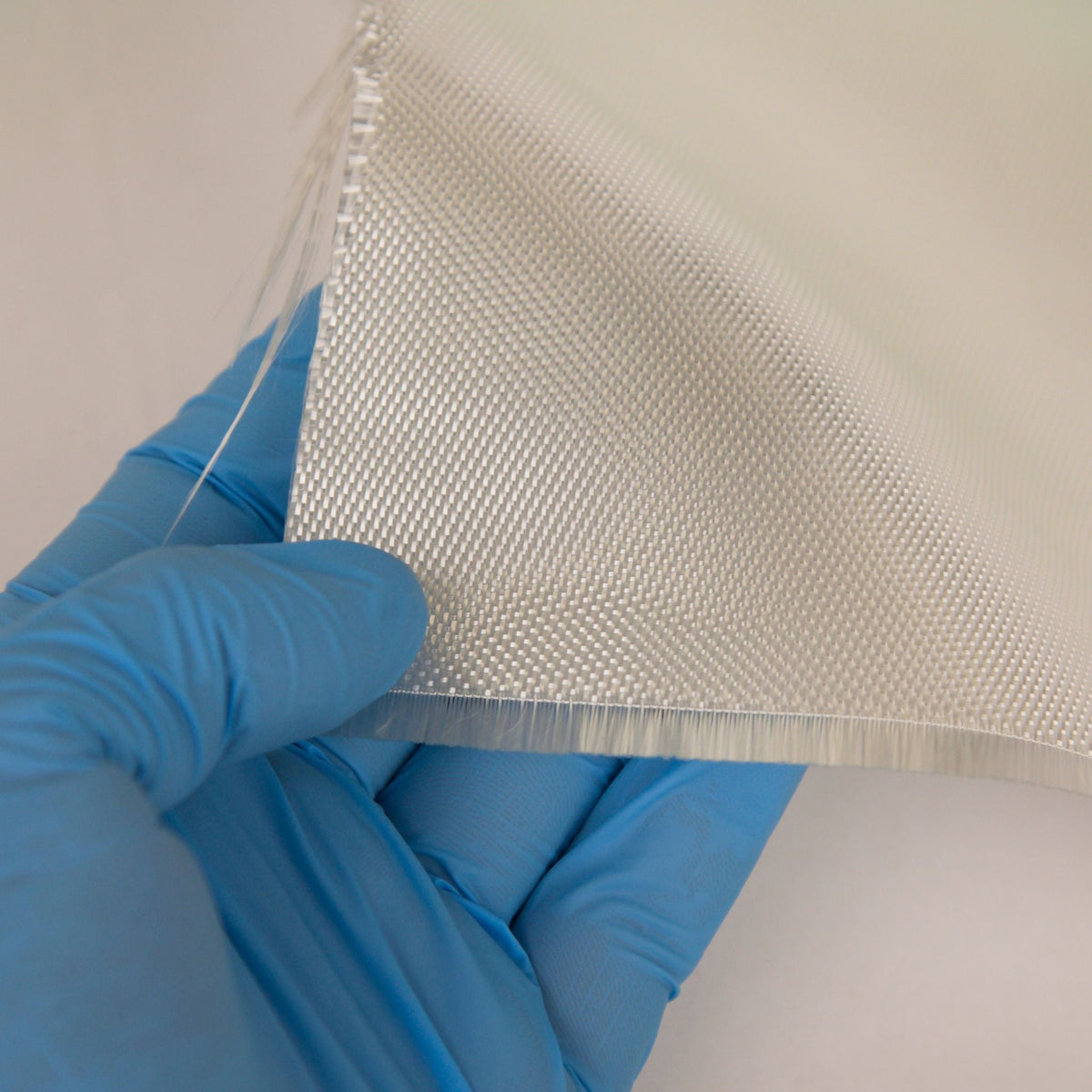 Gloved hand holding the cut edge of satin weave fiberglass cloth